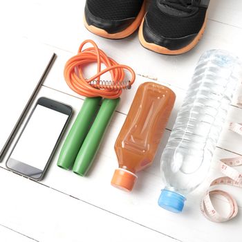 fitness equipment:running shoes,jumping rope,notepad,phone,water,juice and measuring tape on white wood background