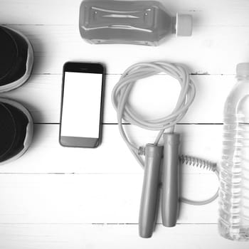 fitness equipment : running shoes,jumping rope,water,juice and phone on white wood background black and white color