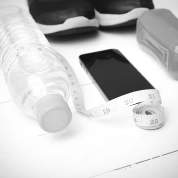 fitness equipment:running shoes,measuring tape,water,juice and phone on white wood background black and white color