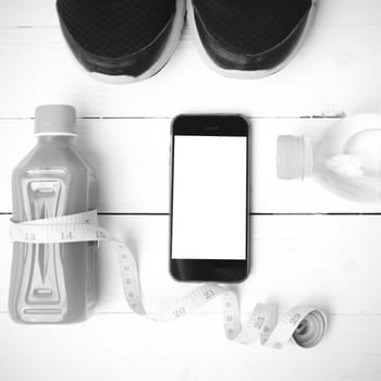 fitness equipment:running shoes,measuring tape,water,juice and phone on white wood background black and white color