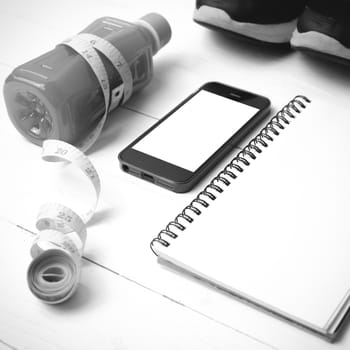 fitness equipment:running shoes,juice,measuring tape,notepad and phone on white wood background black and white color