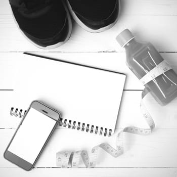 fitness equipment:running shoes,juice,measuring tape,notepad and phone on white wood background black and white color