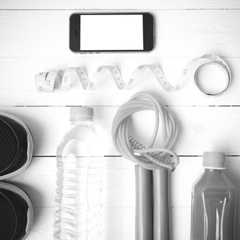 fitness equipment:running shoes,phone,measuring tape,water,juice and jumpong rope on white wood background black and white color