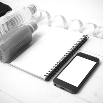 fitness equipment:running shoes,water,measuring tape,notepad,phone and juice on white wood background black and white color