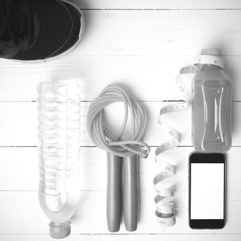 fitness equipment:running shoes,phone,measuring tape,water,juice and jumpong rope on white wood background black and white color