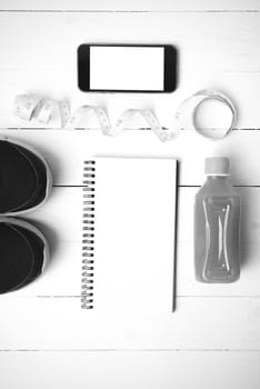 fitness equipment:running shoes,juice,measuring tape,notepad and phone on white wood background black and white color