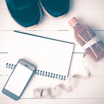 fitness equipment:running shoes,juice,measuring tape,notepad and phone on white wood background vintage style