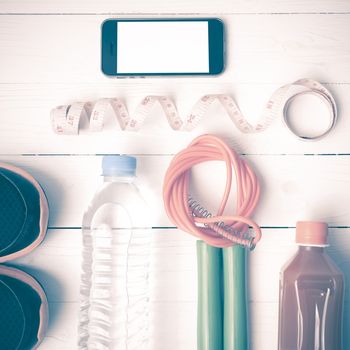 fitness equipment:running shoes,phone,measuring tape,water,juice and jumpong rope on white wood background vintage style