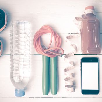 fitness equipment:running shoes,phone,measuring tape,water,juice and jumpong rope on white wood background vintage style