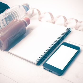 fitness equipment:running shoes,water,measuring tape,notepad,phone and juice on white wood background vintage style