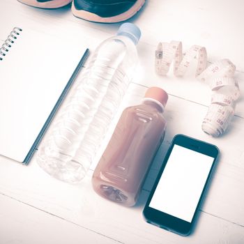 fitness equipment:running shoes,water,measuring tape,notepad,phone and juice on white wood background vintage style