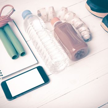 fitness equipment:running shoes,jumping rope,notepad,phone,water,juice and measuring tape on white wood background vintage style