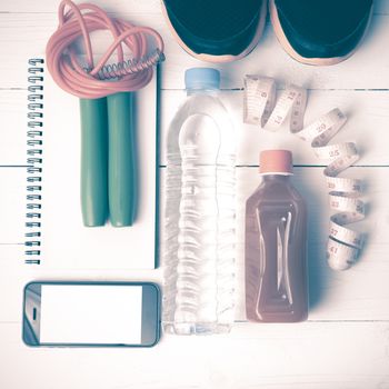 fitness equipment:running shoes,jumping rope,notepad,phone,water,juice and measuring tape on white wood background vintage style