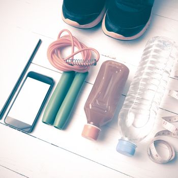 fitness equipment:running shoes,jumping rope,notepad,phone,water,juice and measuring tape on white wood background vintage style