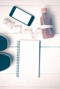 fitness equipment:running shoes,juice,measuring tape,notepad and phone on white wood background vintage style