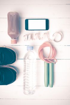 fitness equipment:running shoes,phone,measuring tape,water,juice and jumpong rope on white wood background vintage style