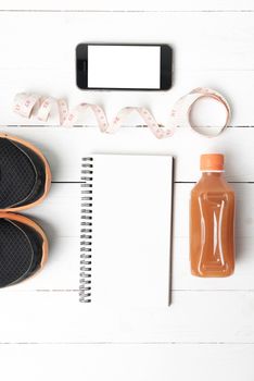 fitness equipment:running shoes,juice,measuring tape,notepad and phone on white wood background