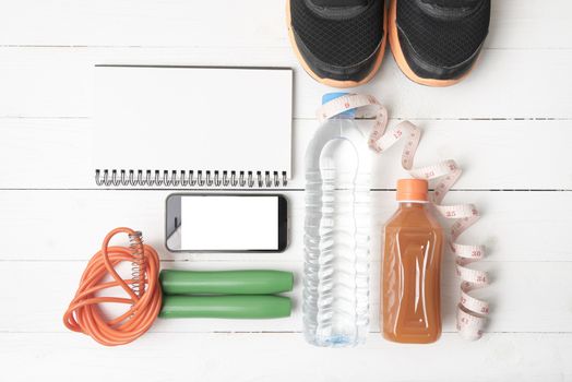 fitness equipment:running shoes,jumping rope,notepad,phone,water,juice and measuring tape on white wood background