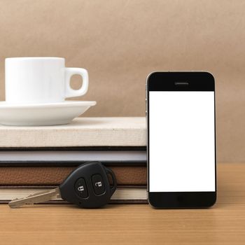 coffee cup with phone car key and stack of book on wood background