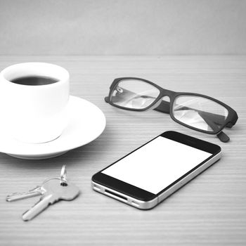 coffee cup and phone with key on wood background black and white color