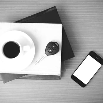 coffee cup with phone car key and stack of book on wood background black and white color