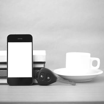 coffee cup with phone car key and stack of book on wood background black and white color