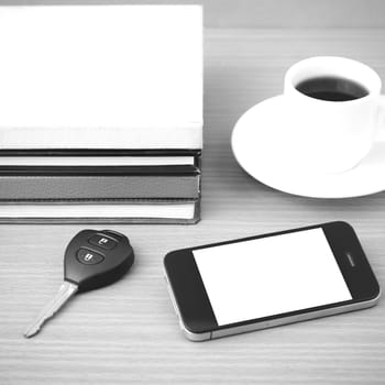 coffee cup with phone car key and stack of book on wood background black and white color