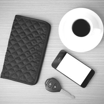 coffee cup with phone car key and wallet on wood background black and white color