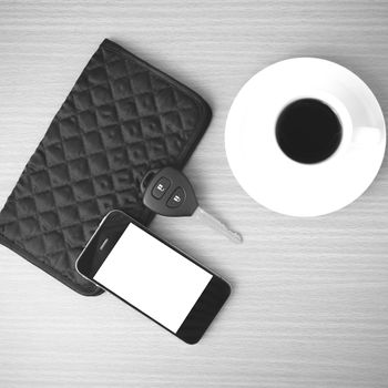 coffee cup with phone car key and wallet on wood background black and white color