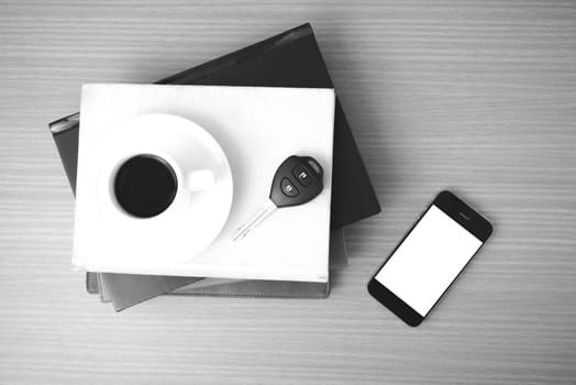coffee cup with phone car key and stack of book on wood background black and white color