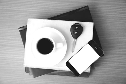 coffee cup with phone car key and stack of book on wood background black and white color