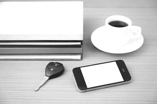 coffee cup with phone car key and stack of book on wood background black and white color