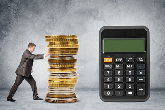 Businessman pushing pile of coins towards calculator