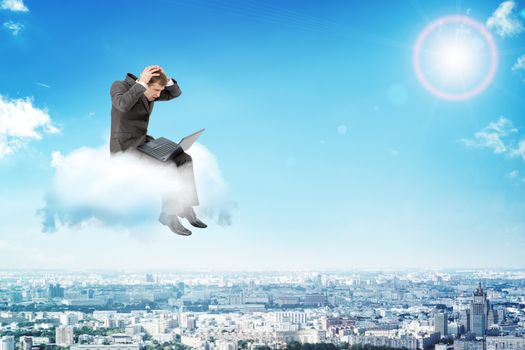 Confused businessman working on laptop and sitting on cloud above city