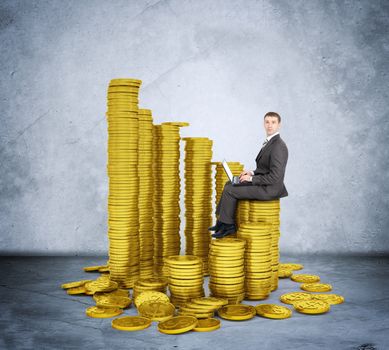 Businessman working on laptop and sitting coins on grey wall background