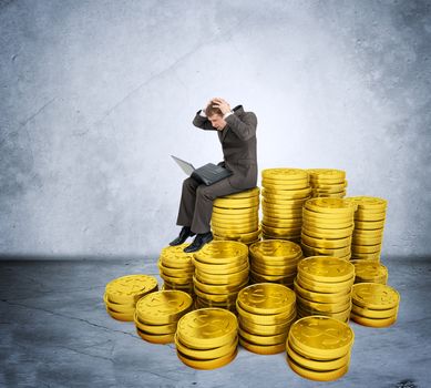 Confused businessman working on laptop and sitting coins on grey wall background