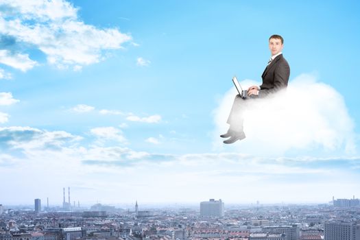 Businessman working on laptop and sitting on cloud above city