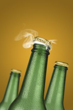 Green cold beer bottle with water drops and golden cap open on yellow background 