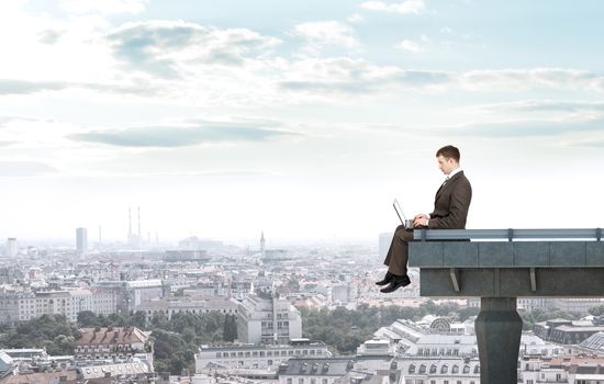 Businessman working on laptop and sitting bridge above city