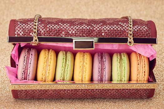 Macarons french in handbag. Luxury shiny glamor fashion clutch. Sweet colorful dessert. Unusual creative art, gold party background, bokeh, closeup. Vintage