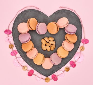 Still life, macarons sweet colorful, heart shape, black placemat. French traditional dessert, almond, necklace. Unusual creative romantic, pink background. Concept for love story. Valentines Day