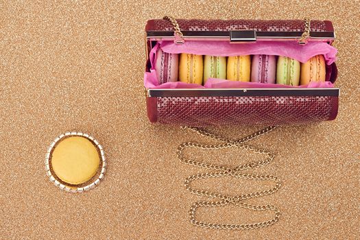 Macarons french in handbag. Luxury shiny glamor fashion clutch. Sweet colorful dessert. Unusual creative art, gold party background, bokeh, copyspase. Vintage