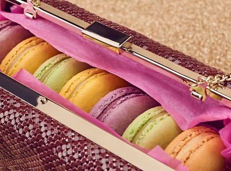 Macarons french in handbag. Luxury shiny glamor fashion clutch. Sweet colorful dessert. Unusual creative art, gold party background, bokeh, closeup. Vintage