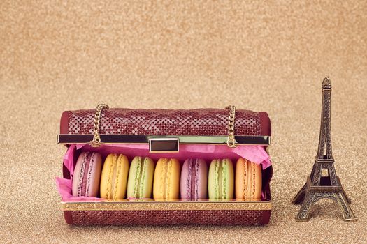 Macarons french in handbag. Eiffel Tower, souvenir Paris. Luxury shiny glamor fashion clutch. Unusual creative art, gold party background, bokeh, closeup. Still life, vintage