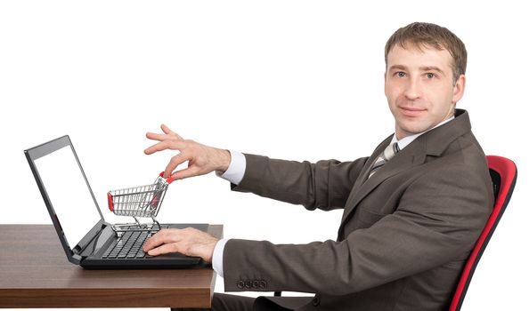 Businessman giving shopping cart to laptop and looking at camera isolated on white background