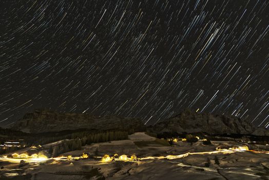 Star trails over Sasso della Croce and La Varella mountains of the Alta Badia in the Dolomites with blue sky background, winter season - Italy