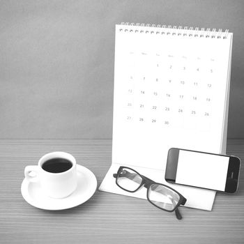 coffee,phone,eyeglasses and calendar on wood table background black and white color