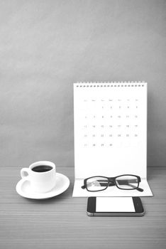 coffee,phone,eyeglasses and calendar on wood table background black and white color