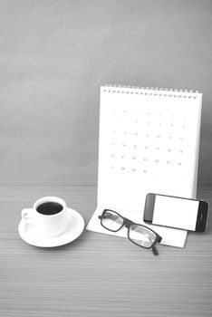 coffee,phone,eyeglasses and calendar on wood table background black and white color