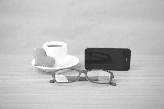 coffee,phone,eyeglasses and heart on wood table background black and white color